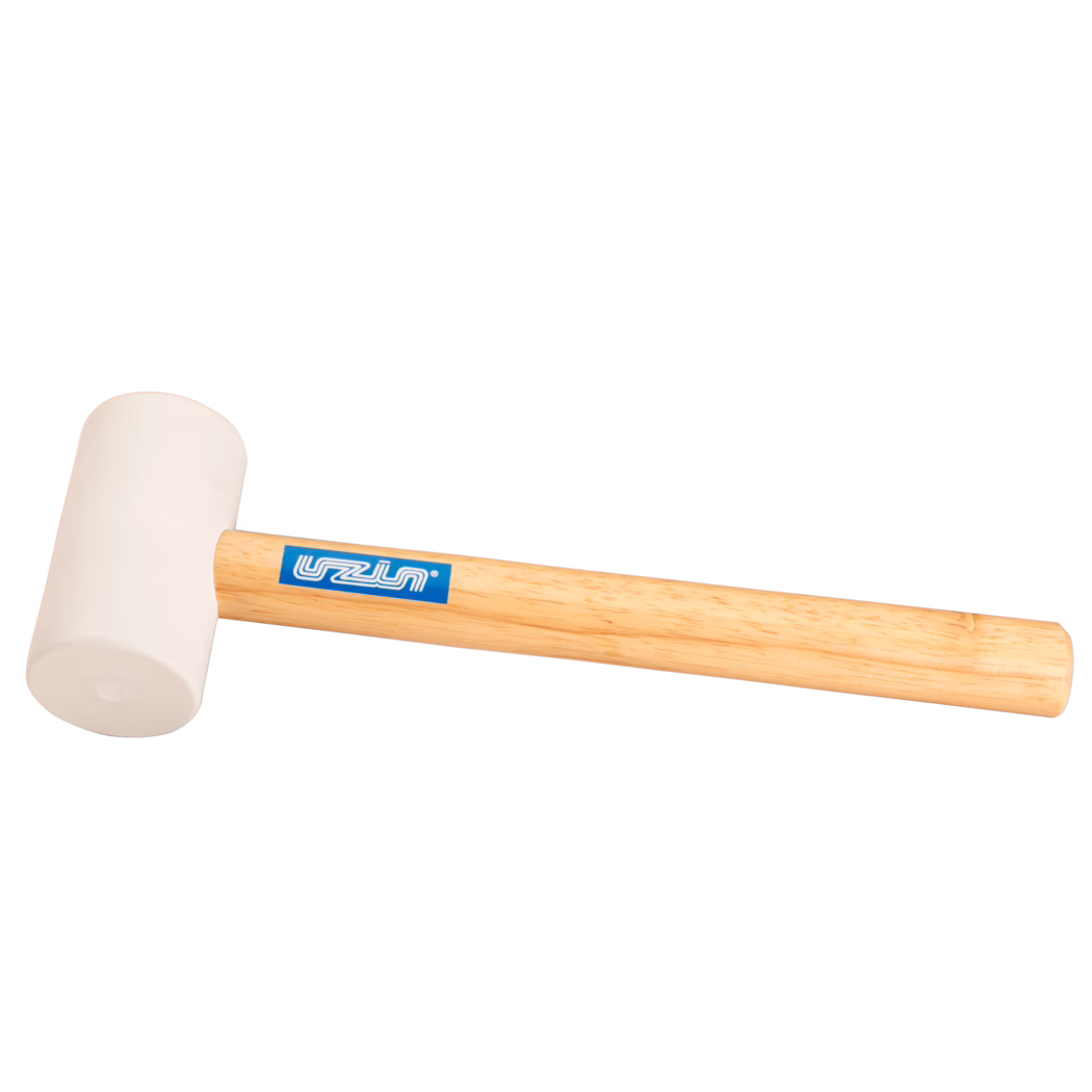 UZIN_Dummy_rubber hammer-UZIN_2014-11 Närbild på produkt: gummihammare med ljusbeige gummihuvud monterat på ett slätt ljust trähandtag med en blå rektangulär märklapp; verktyget ligger diagonalt mot en vit bakgrund, mjuk jämn belysning framhäver gummits struktur och träets ådring; lämpad för försiktiga slag vid snickeri, montering eller läggning av kakel.